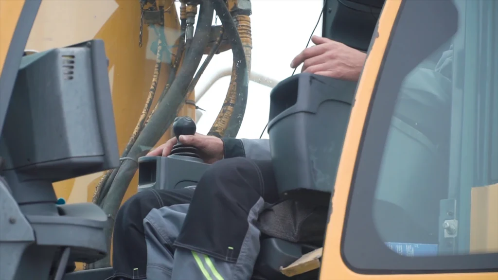 Opérateur d’engin de chantier manipulant le joystick d’une grue hydraulique depuis la cabine.