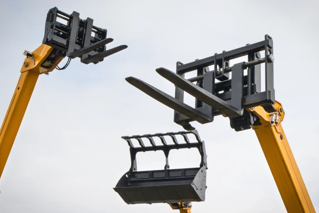 Accessoires de chargeuse sur chantier : fourches palettes, godet et grappin hydraulique montés sur bras jaune