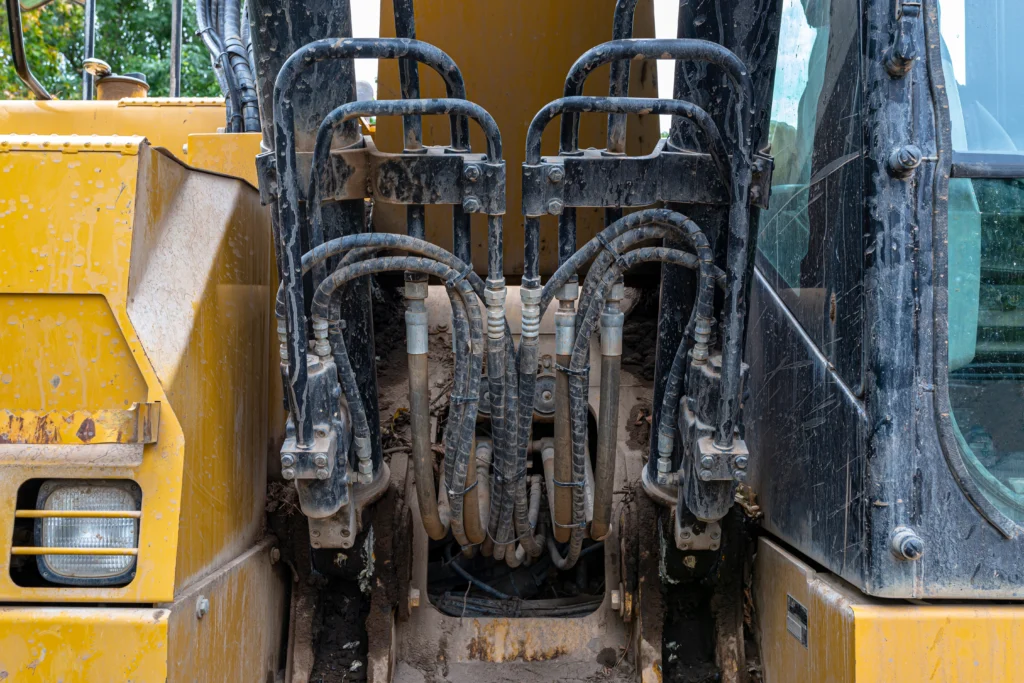 Détail des composants hydrauliques d’une pelle mécanique, avec flexibles, vérins et raccords métalliques.