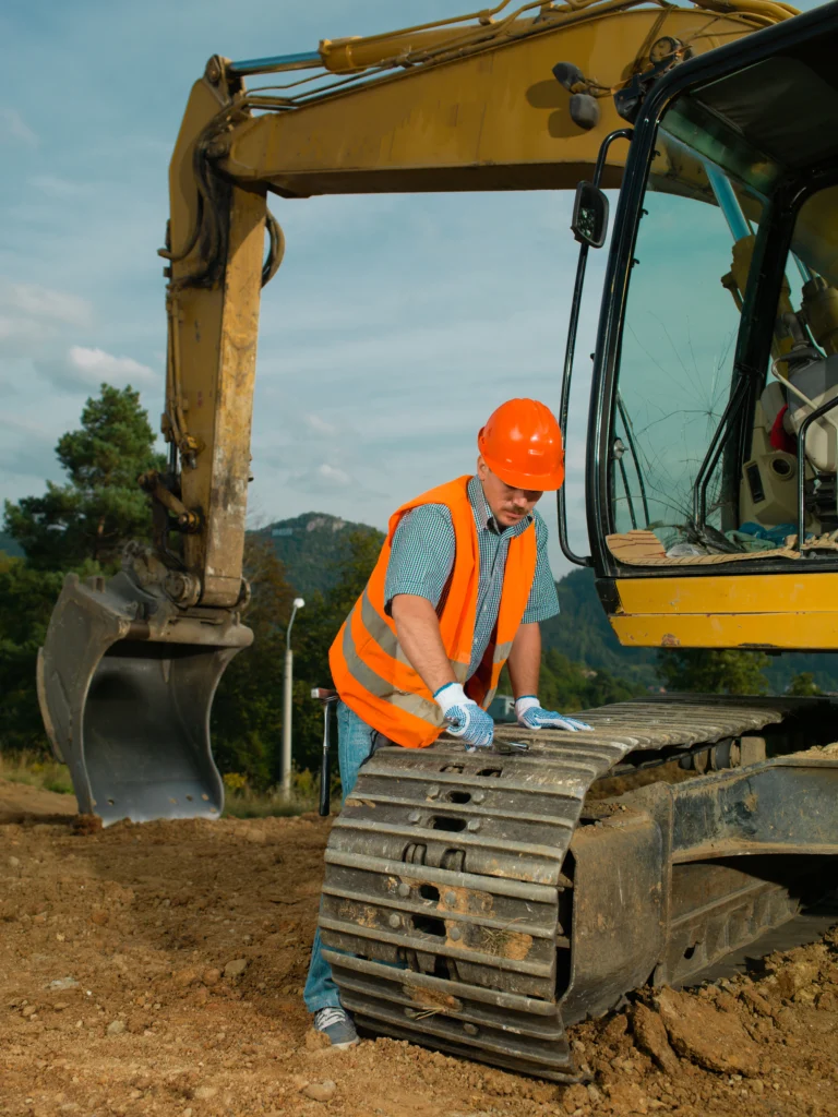 Technicien en équipement de chantier réparant la chenille d’une pelleteuse pour assurer sécurité et conformité.