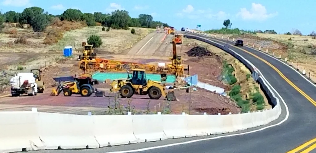 Chantier de construction routière avec grue mobile sur camion et engins de terrassement travaillant sur nouvelle bretelle d'autoroute