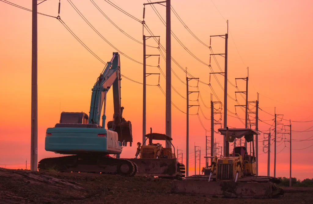 Silhouette d’une pelleteuse et de deux bulldozers stationnés sur un chantier.