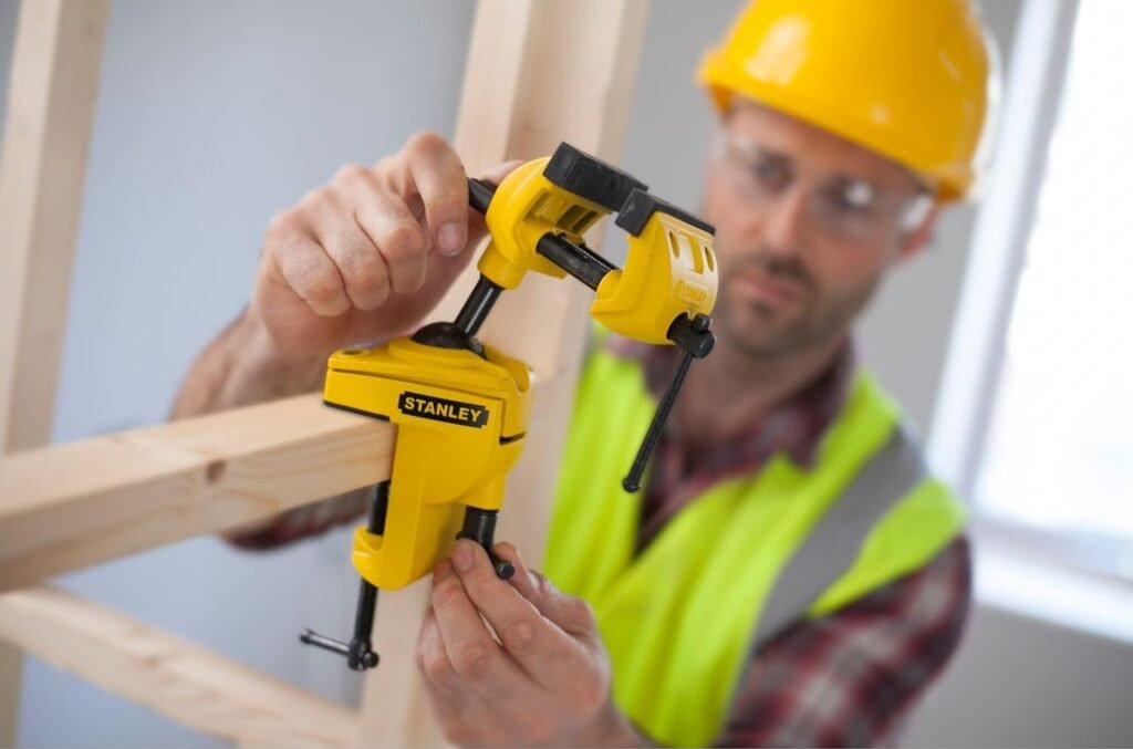 Étau Stanley MAXSTEEL multi-angle avec système de rotule 360° serrant une pièce métallique sur établi d'atelier professionnel